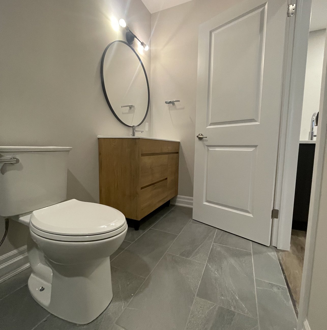 renovated bathroom with wood vanity and grey tile floor in a Woodstock ON home