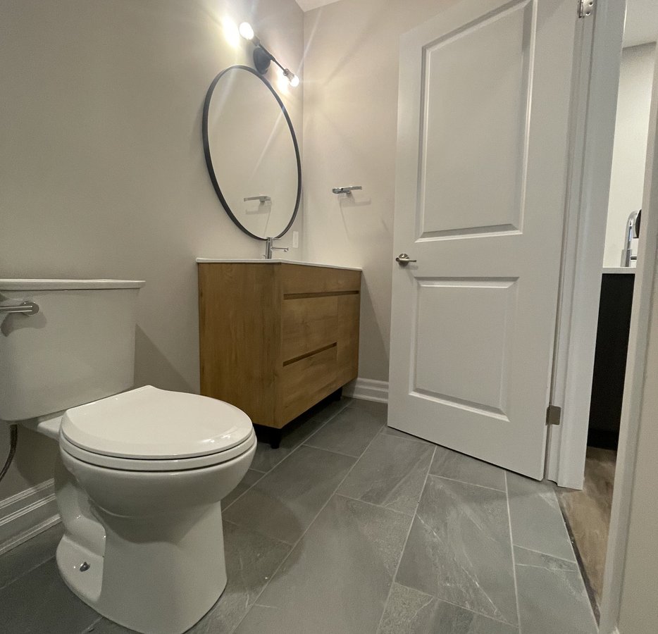 renovated bathroom with wood vanity and grey tile floor in a Woodstock ON home